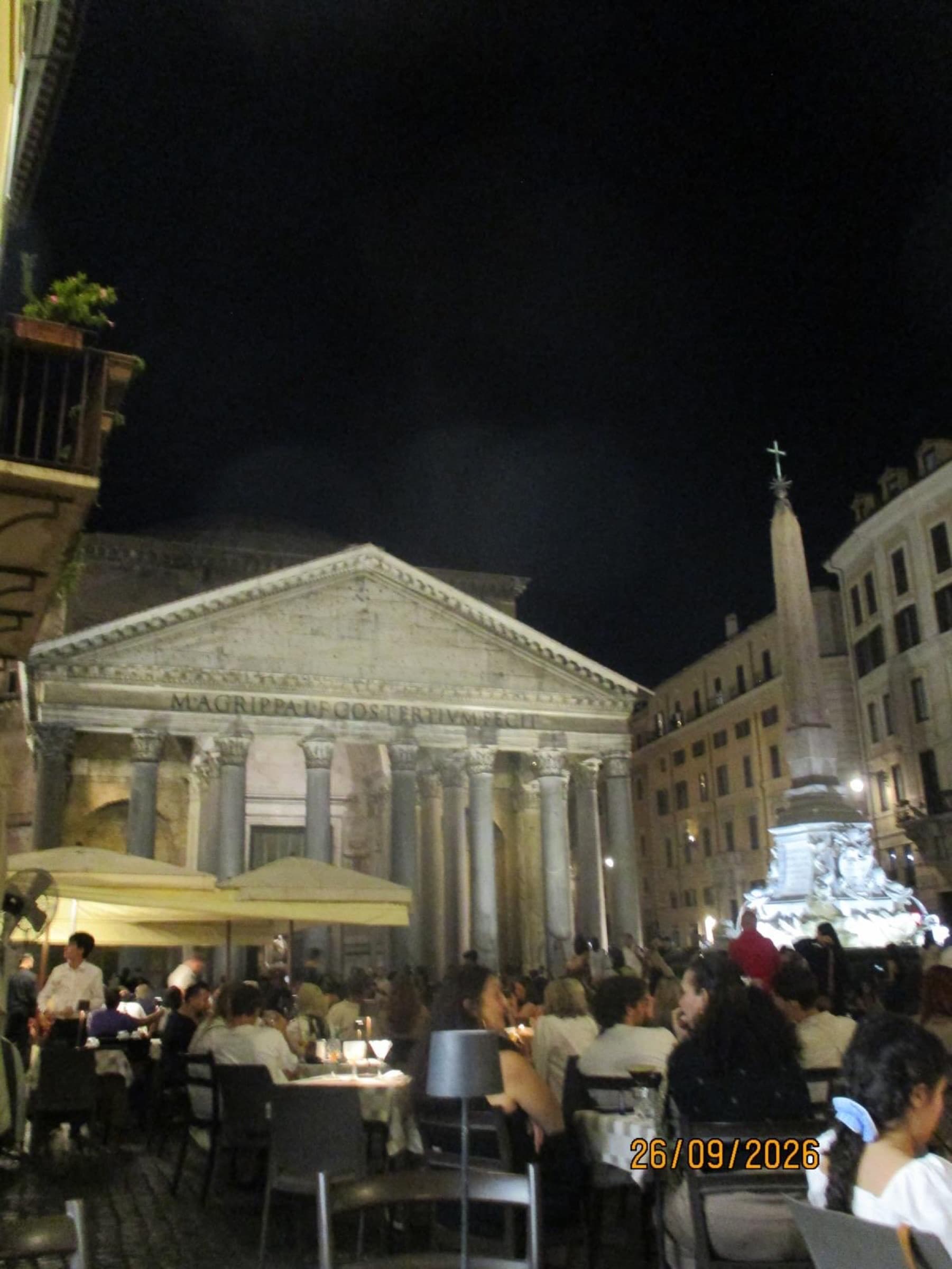 The Pantheon lit up at night above crowded café tables