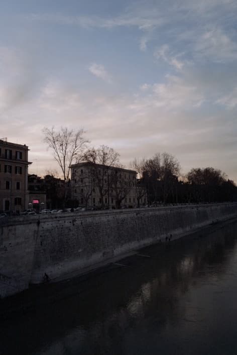 The stone embankment of the Tiber under a soft evening sky